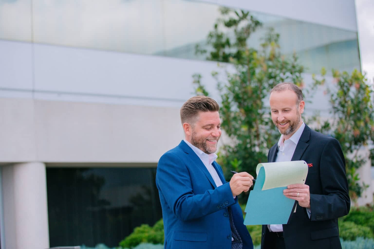 Two business colleagues discussing documents outdoors in front of a modern building.