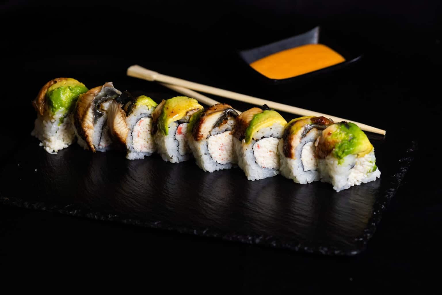 Sushi rolls on slate with dipping sauce, culinary photography.