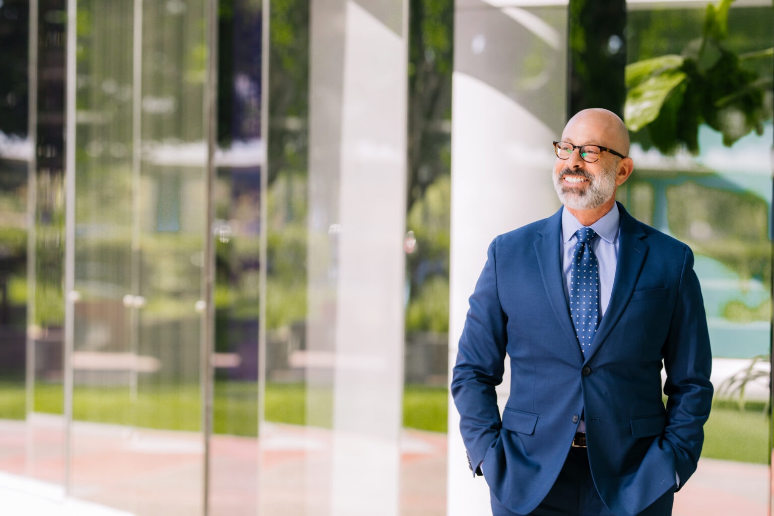 Professional business portrait of a man in a blue suit standing beside a large office window