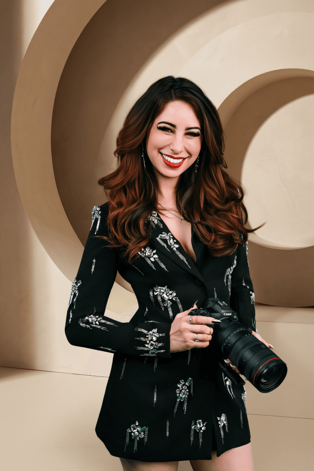 Woman holding a professional camera, standing in front of a beige geometric background capturing the style and expertise of Southern California’s best photographer for branding shoots.